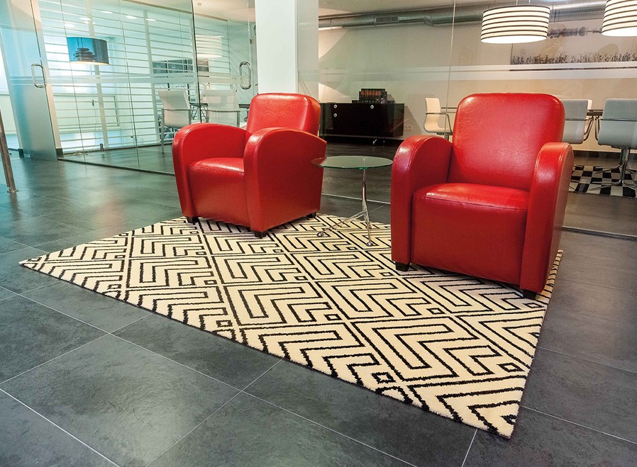 Imagen de una alfombra con dibujos geométricos, en un salón moderno, con dos sillones rojos y una mesita
